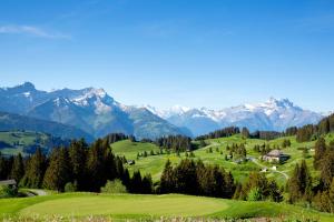 a green golf course with mountains in the background at Victoria Hotel & Residence in Villars-sur-Ollon +111 photos