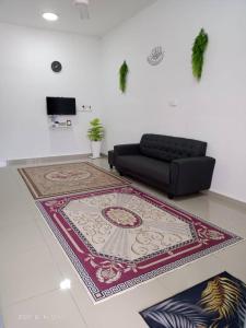 a living room with a black couch and a rug at Dina Homestay B in Pasir Puteh