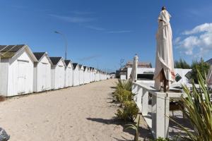 una fila de cabañas de playa blancas con sombrilla en Gîte à 3 minutes à pied de la mer en Bernières-sur-Mer