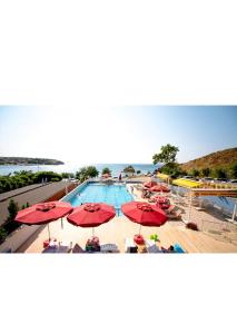 - une piscine avec des parasols et des chaises rouges et l'océan dans l'établissement Mercan Otel, à Çanakkale