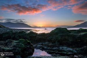 a sunset on the beach with rocks and water at The Little Red Door in Warrenpoint
