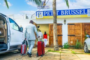 un uomo che cammina con i bagagli davanti a un edificio di Hotel Petit Brussel a Lomé