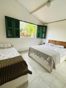 a bedroom with two beds and green shuttered windows at Pousada Vila Matury in Icapuí