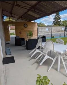 un patio con sillas blancas, una mesa y un reloj en Maison 5 personnes en Mansigné