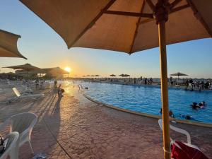 ein Pool mit Sonnenschirm und Menschen im Wasser in der Unterkunft Yahia Blumar North Coast in El-Alamein