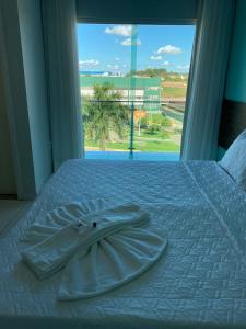 a white bed with a robe on it with a window at Gênova Palace Hotel in Acailandia