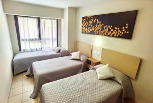 a hotel room with three beds and a window at HOSTAL RIGAU in Sant Feliu de Guíxols