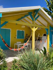a yellow and blue shack with a hammock in front at Les Cauris de l'Anse in Sainte-Anne