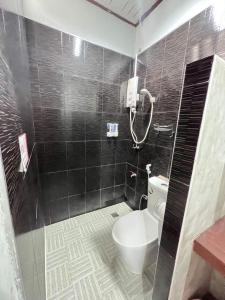 baño de azulejos negros con aseo y ducha en The Sekret Hotel, en Sungai Kolok