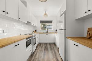 a white kitchen with wooden floors and white cabinets at Wanderer by Experience Jervis Bay in Sanctuary Point