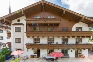 a large wooden building with a balcony and red umbrellas at Pension Appartements Alpenblick in Maria Alm am Steinernen Meer