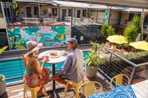 dos personas sentadas en una mesa junto a una piscina en YHA Byron Bay, en Byron Bay