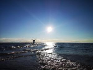 a person standing in the ocean with their arms up at Northern Lights - Cozy apartment, sisältää liinavaatteet in Kalajoki