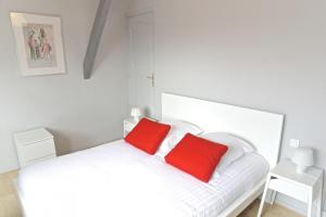 a white bed with two red pillows on it at Chartres - Appartement 1 chambre avec ascenseur in Bordeaux