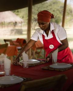 a woman is standing at a table with plates at Lake Natron Maasai giraffe eco Lodge and camping in Mtowabaga