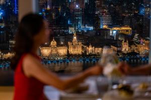 a woman in a red dress looking at the city at night at The Ritz-Carlton Shanghai, Pudong in Shanghai
