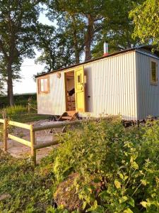 a small white shed with a yellow door in a yard at The Hereford Hut, Charming 1 bedroom Shepherds Hut in Callow