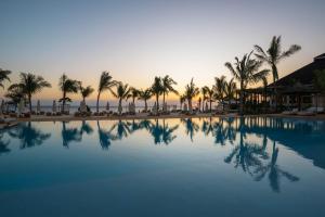 a swimming pool with palm trees and a sunset at Aldiana Club Zanzibar Kwanza in Kizimkazi
