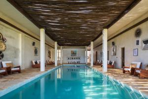 a swimming pool with chairs and a wooden ceiling at Aldiana Club Zanzibar Kwanza in Kizimkazi