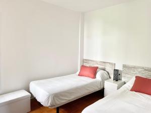 Duas camas num quarto com paredes brancas e almofadas vermelhas em Luminoso apartamento frente al mar con piscina em Roses