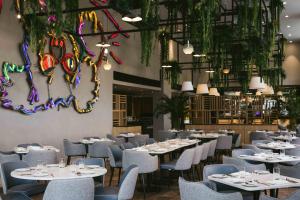 a restaurant with white tables and chairs and plants at Martinhal Lisbon Oriente in Lisbon