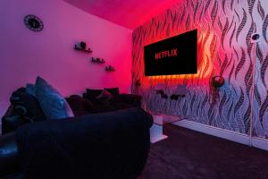 65 inch TV in Modern 2 Bed Hideaway في برادفورد: غرفة معيشة مع أريكة في غرفة وردية