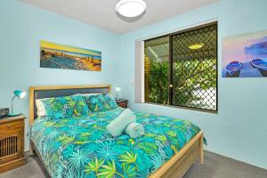 a bedroom with a bed with a blue bedspread and a window at Tee Jays in Sawtell