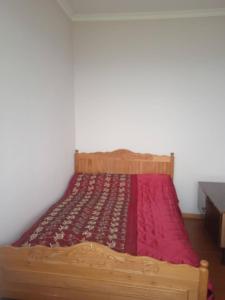un letto in legno con una coperta rossa sopra di Чкалов гостевой дом a Chʼkalov