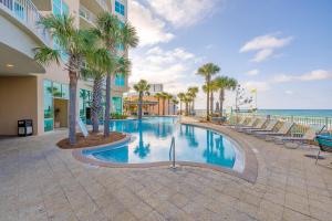 a swimming pool with palm trees and the ocean at Totally Beach'n at 1605 Aqua in Panama City Beach
