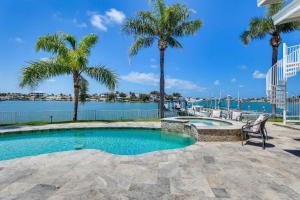 a swimming pool with palm trees next to a body of water at Luxury St Petersburg Home with Pool and Bay Access! in St Pete Beach