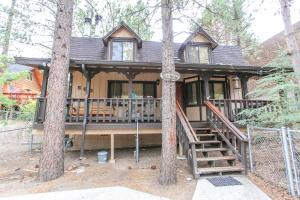 Una casa en el bosque con un porche y dos árboles. en Mountain Bliss - Semi-secluded woodsy quiet cabinm, covered deck with a porch swing!, en Big Bear City