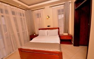 a bedroom with a bed with white sheets and windows at Casabonita Villas in Kampala