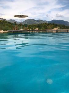 a large pool of blue water with an umbrella at Botë Farms Agriturismo in Sarandë