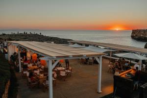a restaurant on the beach with a sunset in the background at VORAMAR by 3VILLAS in Cala en Forcat
