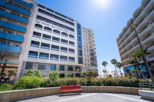 a red bench in front of a tall building at Hotel Spa Cádiz Plaza in Cádiz