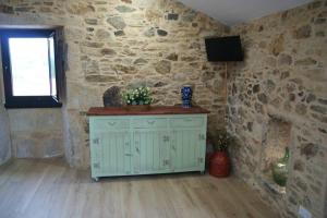 a room with a stone wall with a cabinet and a television at Casa de Busto in Zas