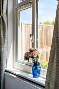 un jarrón azul con flores sentado en el alféizar de la ventana en Lovely garden apartment in Wimbledon Town Centre with private parking by Wimbledon Holiday Lets, en Londres