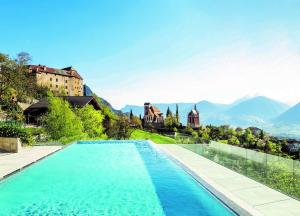 a swimming pool with a castle and mountains in the background at Hotel Finkennest - Panoramic Garden Resort in Schenna