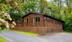 a wooden cabin with a fence in front of it at Charming Copse Corner Lodge - Spa Resort - Devon in Chudleigh