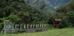 a sign in a field with a mountain in the background at QUECHUA´S HOUSE Hostal & Coffee in Machu Picchu