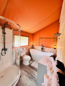 baño de color naranja con bañera, aseo y lavamanos en Tropical glamping with hot tub, en Cleveland