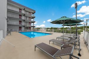 un patio con piscina, sillas y sombrilla en Red Roof PLUS & Suites Virginia Beach - Seaside en Virginia Beach