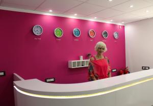 a woman standing in front of a pink wall with clocks at Luwiana Suites in Ljubljana