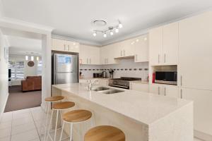a kitchen with white cabinets and a counter with stools at Government Rd 77 Shoal Bay in Shoal Bay