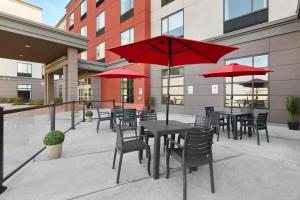 eine Terrasse mit Tischen, Stühlen und roten Sonnenschirmen in der Unterkunft Four Points by Sheraton Sherwood Park in Sherwood Park