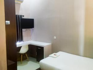 a room with a bed and a desk and a tv at RedDoorz Syariah near Sultan Syarif Kasim II Airport in Pekanbaru