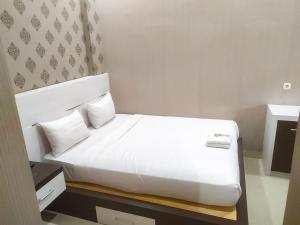 un letto bianco in una camera d'albergo con lenzuola e cuscini bianchi di RedDoorz Syariah near Sultan Syarif Kasim II Airport a Pekanbaru