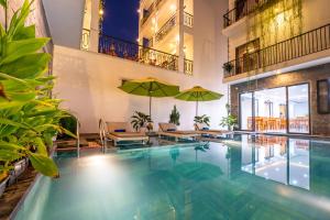 una piscina con mesas y sombrillas en un edificio en Tomorrow Oasis Boutique Villa Hoi An, en Hoi An