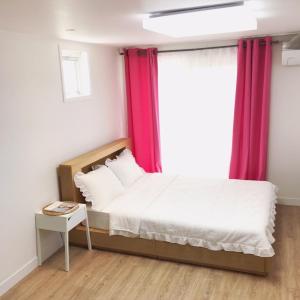 a bedroom with a bed and a window with red curtains at Cozy House & Tour in Jeju