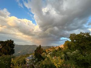 a cloudy sky with trees and houses on a hill at Wincliff Orchard Resort in Mukteshwar